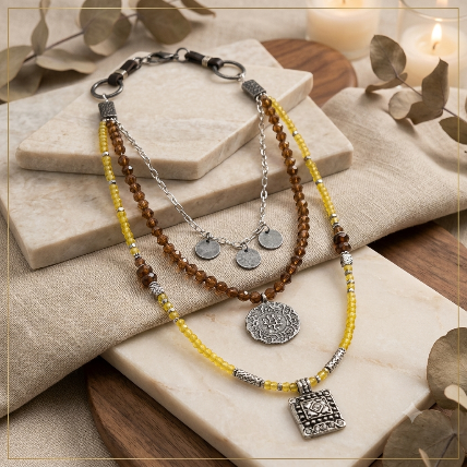 Bohemian layered Eden Garden Waterfall Necklace with brown beads, yellow beads and silver charms displayed on beige stone slabs.